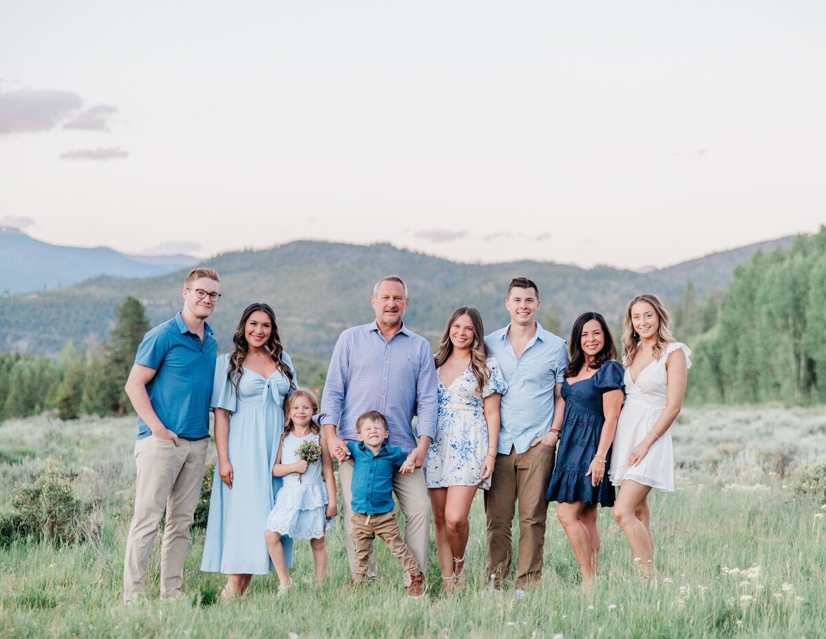 An extended family stands in an open mountain meadow smiling