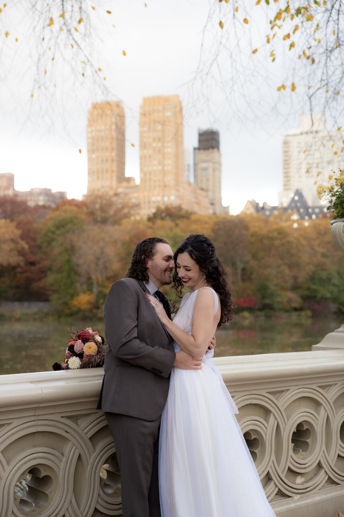 The couple holding hands and smiling as they walk through a peaceful Central Park path.