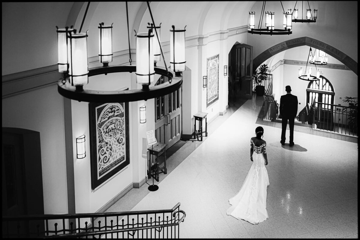 Elegant black and white photo of a bride and groom standing apart in a grand hall