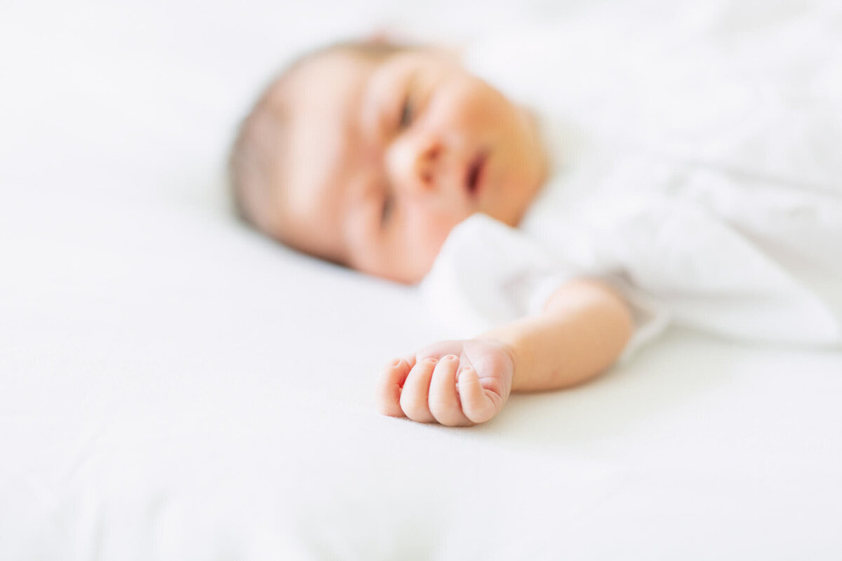 Hand feature of baby girl laying on a bed in a white romper