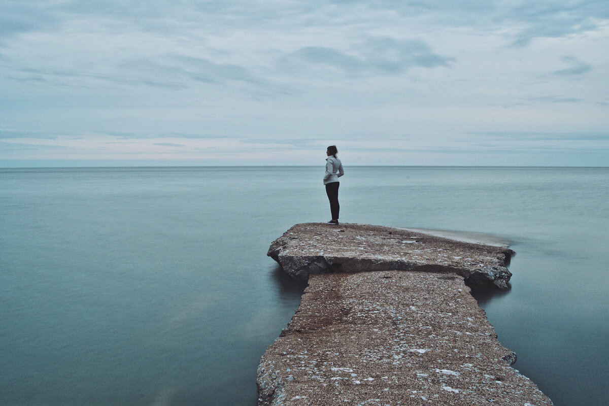 A woman stands by the edge of Lake Erie, taking in the serene landscape and peaceful atmosphere.