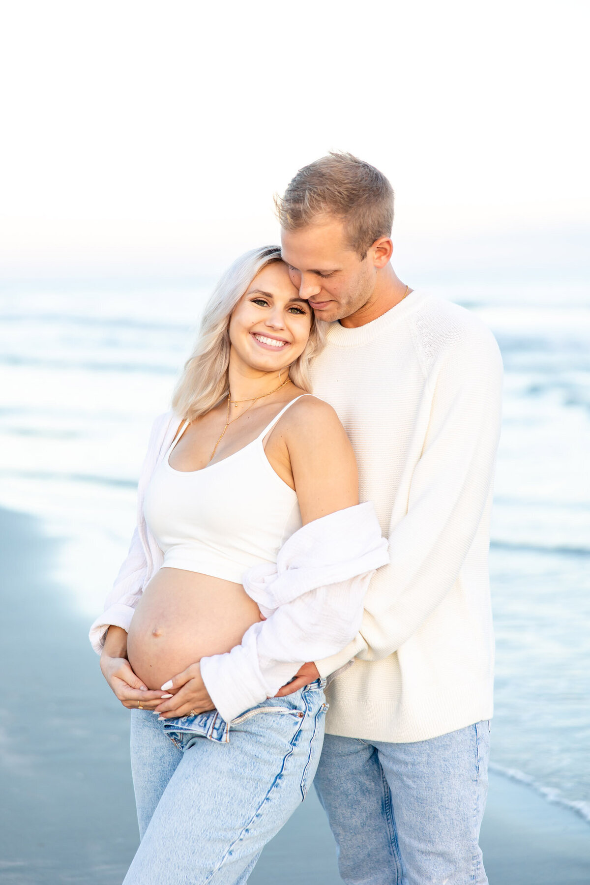 Man holding his pregnant partners belly as they stand by the ocean