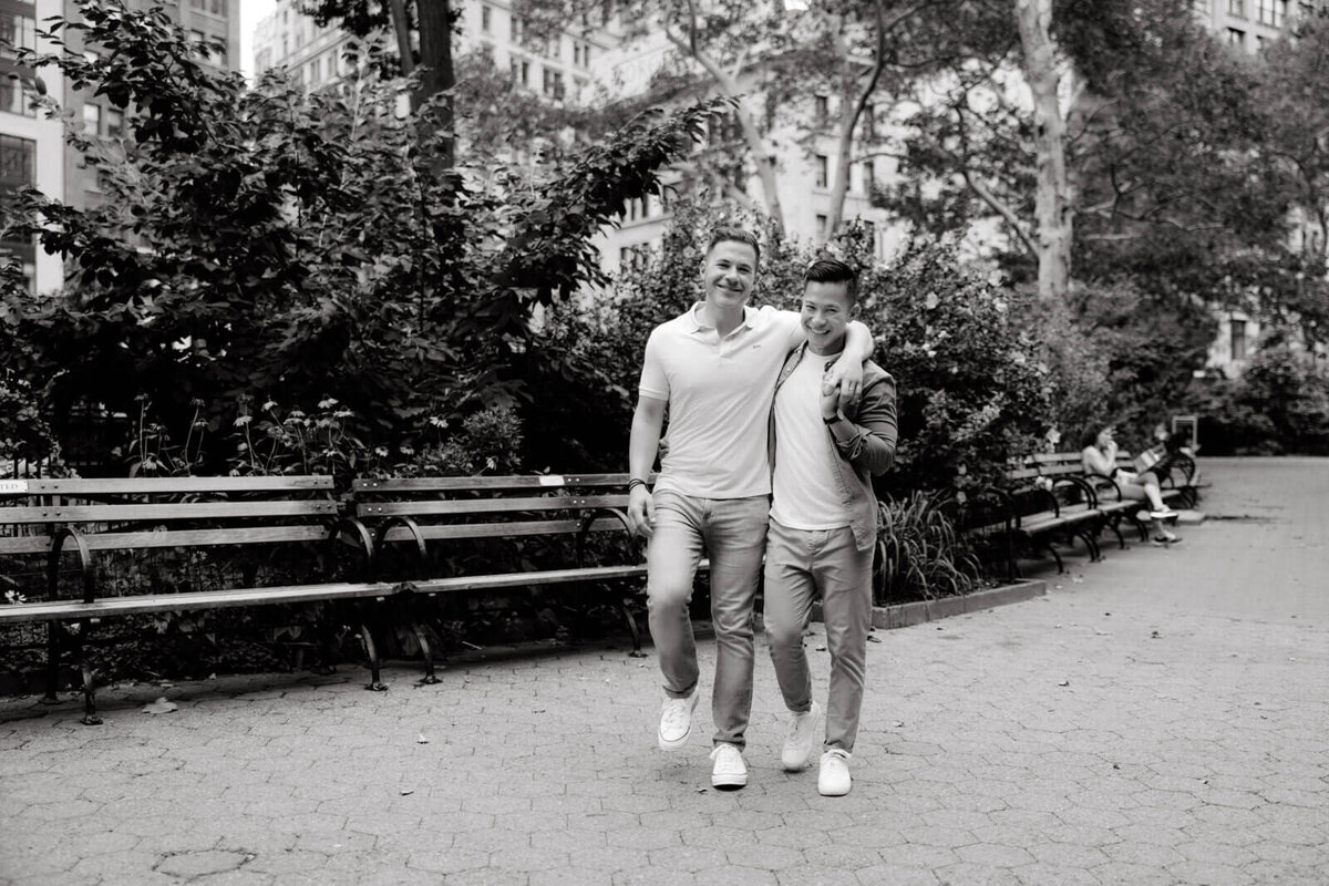Black and white photo of the engaged couple happily walking in a park in West Village, NYC. Image by Jenny Fu Studio.
