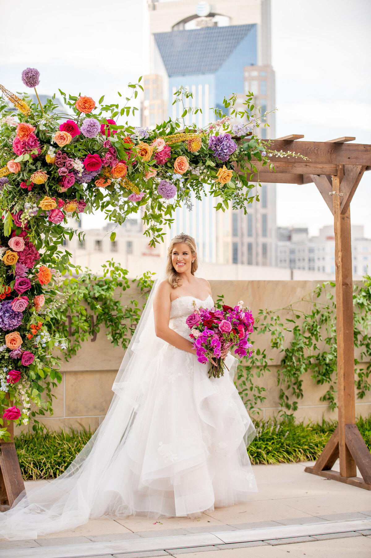 Artful ceremony arch florals in sunset hues of pink, fuchsia, lavender, and orange composed of hydrangeas, delphinium, eremurus, snapdragon, and petal heavy roses. Design by Rosemary and Finch in Nashville, TN.