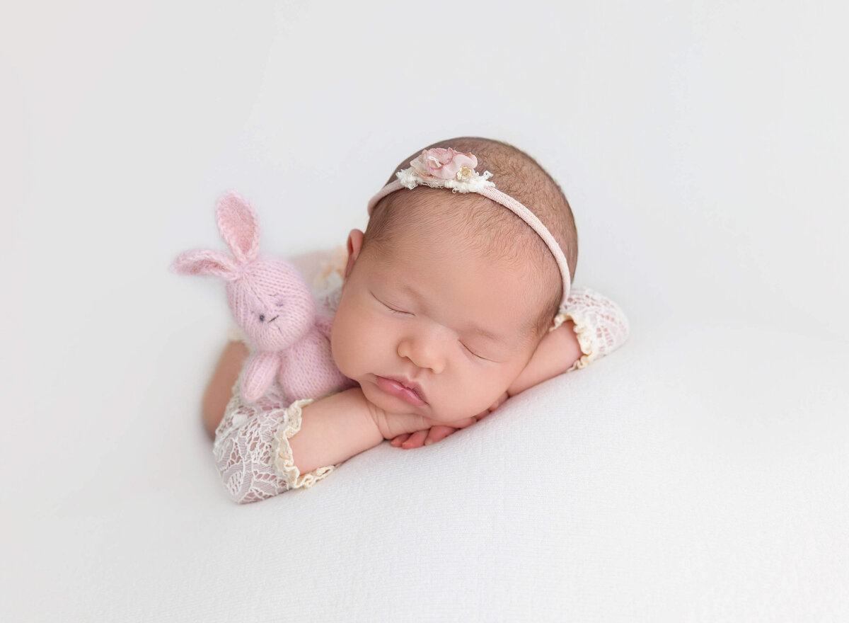 Newborn baby girl in a pink lace outfit, gently holding a pink bunny, captured after her newborn photoshoot in Manhattan, creating a sweet and timeless memory of her first moments.