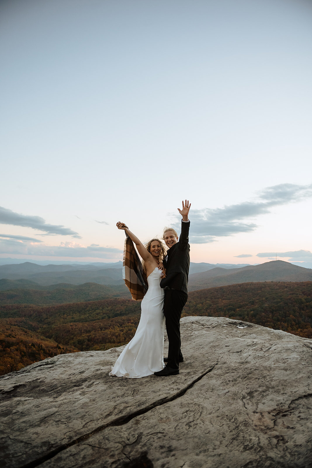 Bride & groom with their hands in the air overlooking the Blue Ridge Mountains at sunset!