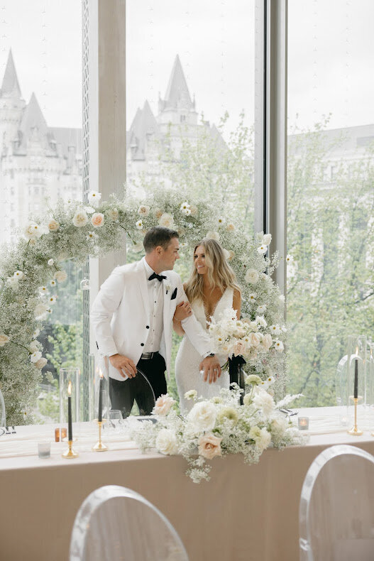 A couple kisses in front of a stunning floral arch during their wedding at the National Arts Centre's O'Born Room, overlooking downtown Ottawa.