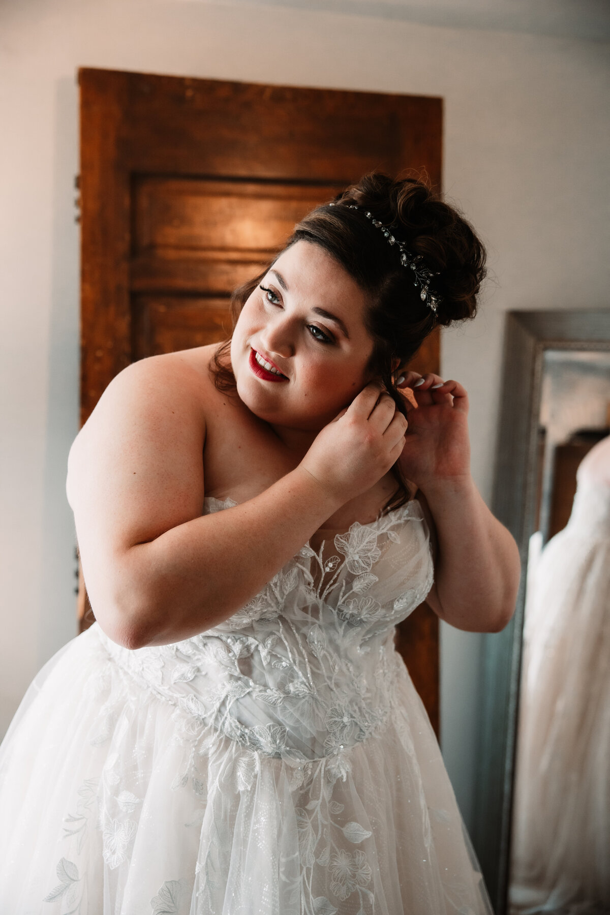 A bride in her dress puts on her earrings in a mirror