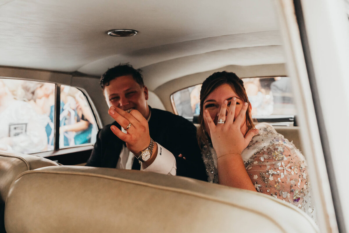 bride and groom show off their rings as they get into their vintage getaway car.
