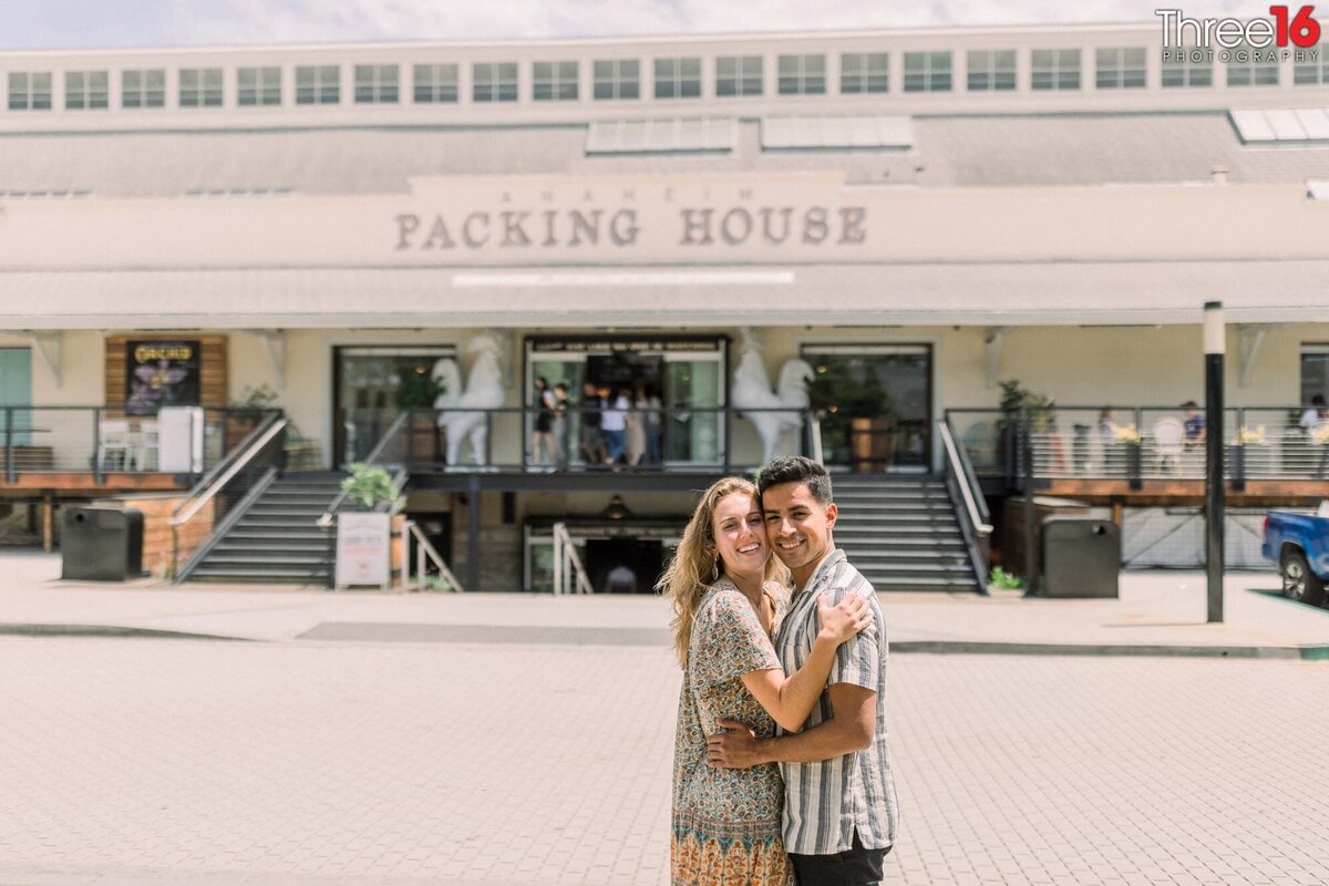 Engaged couple embrace one another during and engagement photo session at the Anaheim Packing District