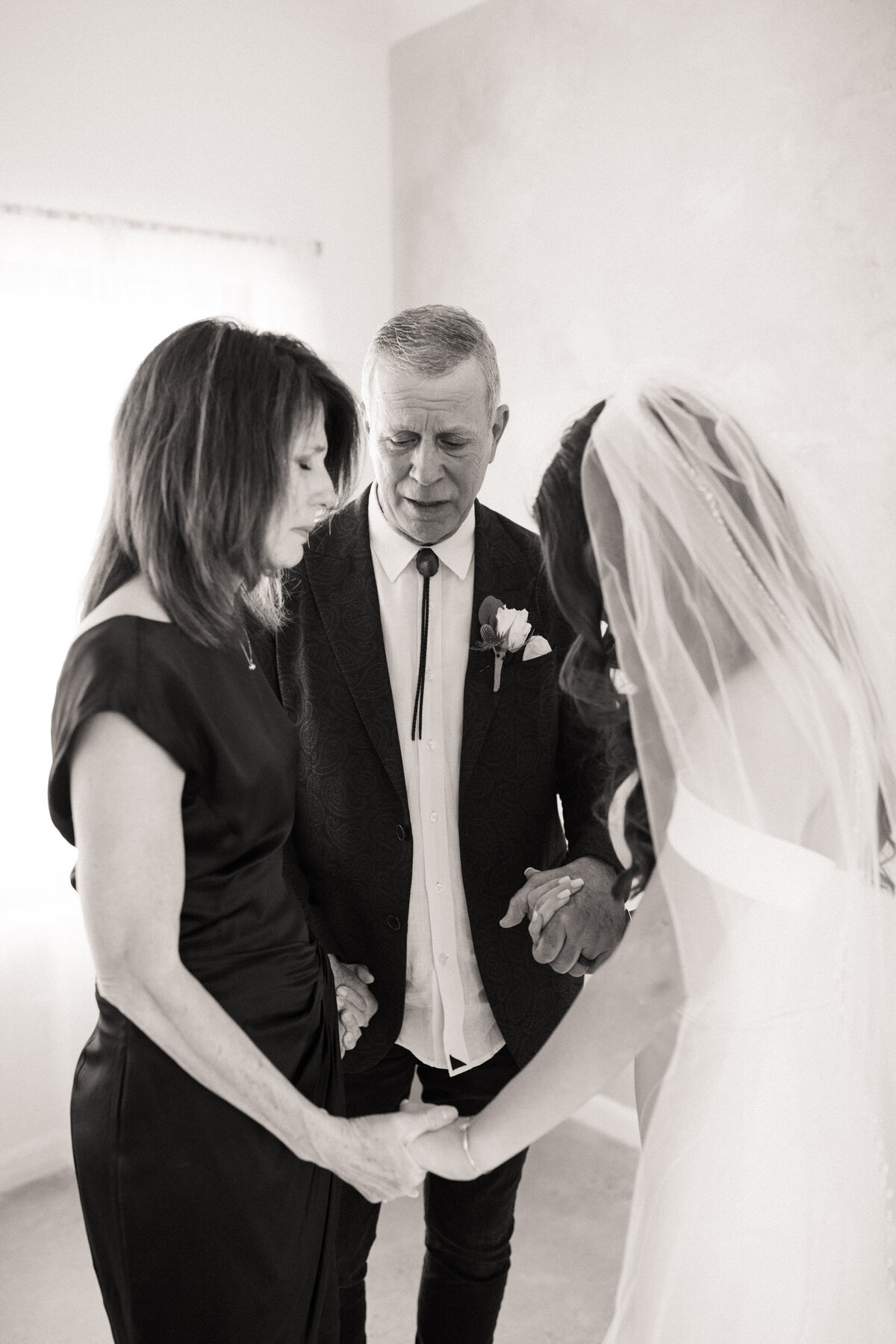 Bride holding hands and praying with her mom and dad during the parent prayer before her wedding ceremony