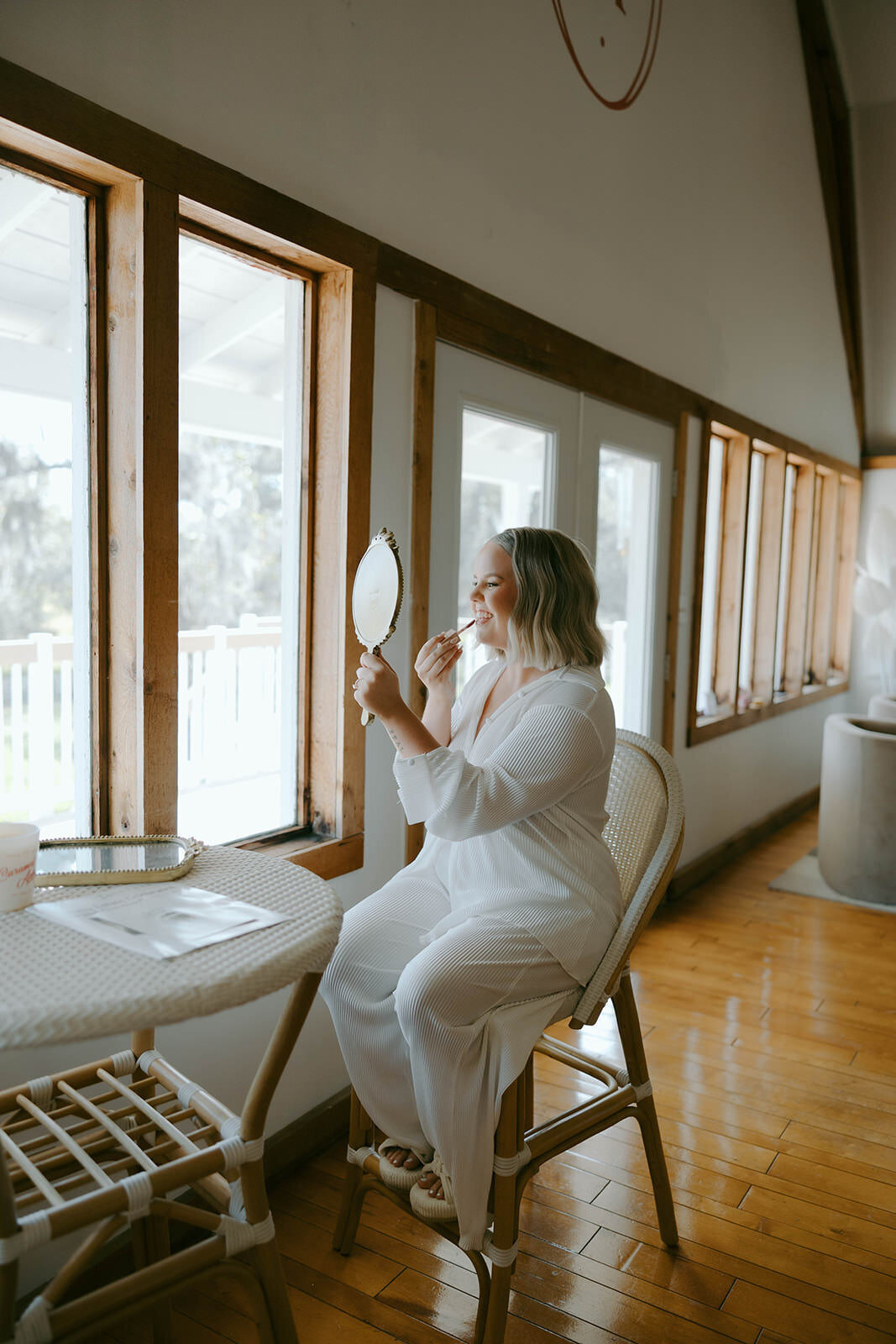 Bride getting ready by a sunlit window in the getting ready room at Uliana Estate in Lakeland Florida.