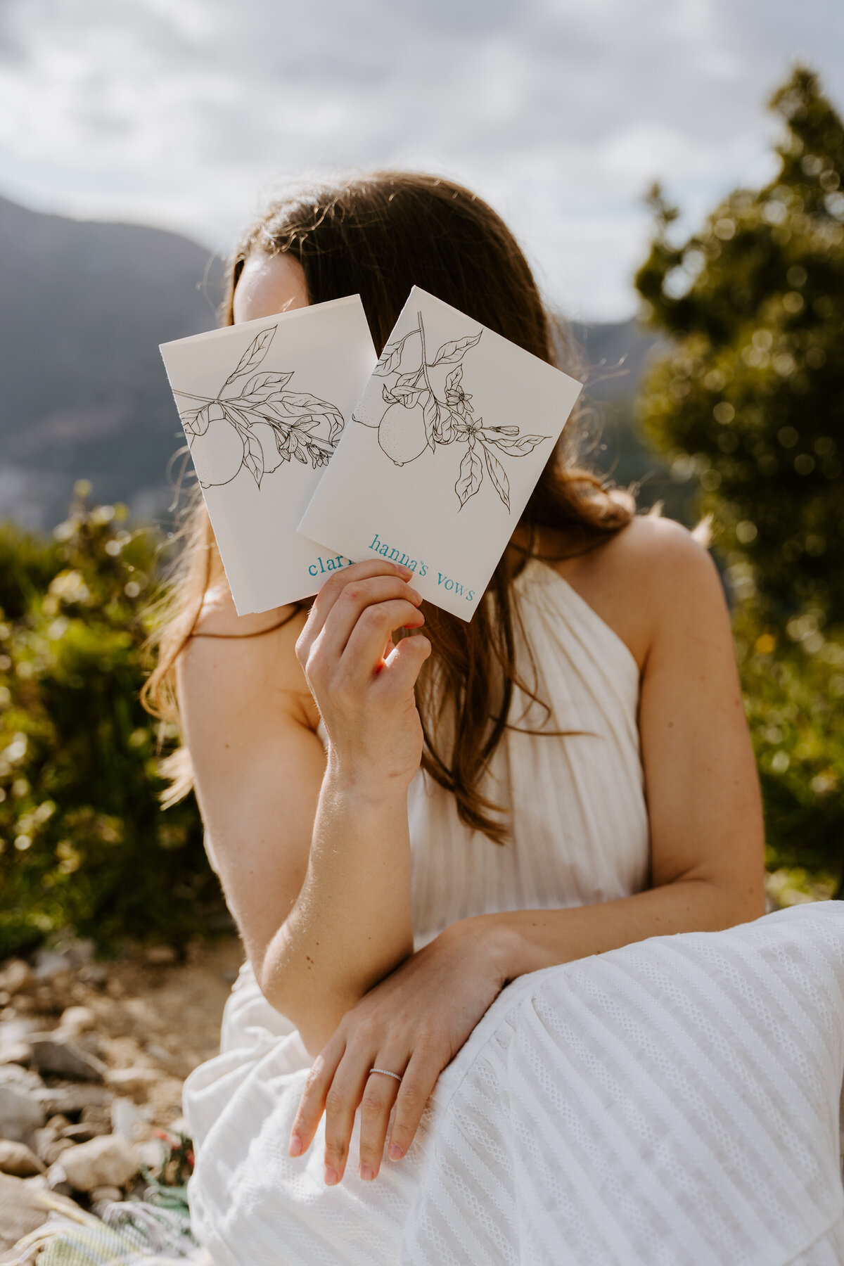 Bride holding ceremony cards with mountain backdrop.
