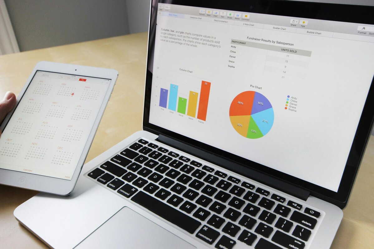 PPC management services being handled on a grey laptop, with the marketer reviewing statistics on the screen and holding a small iPad in hand.