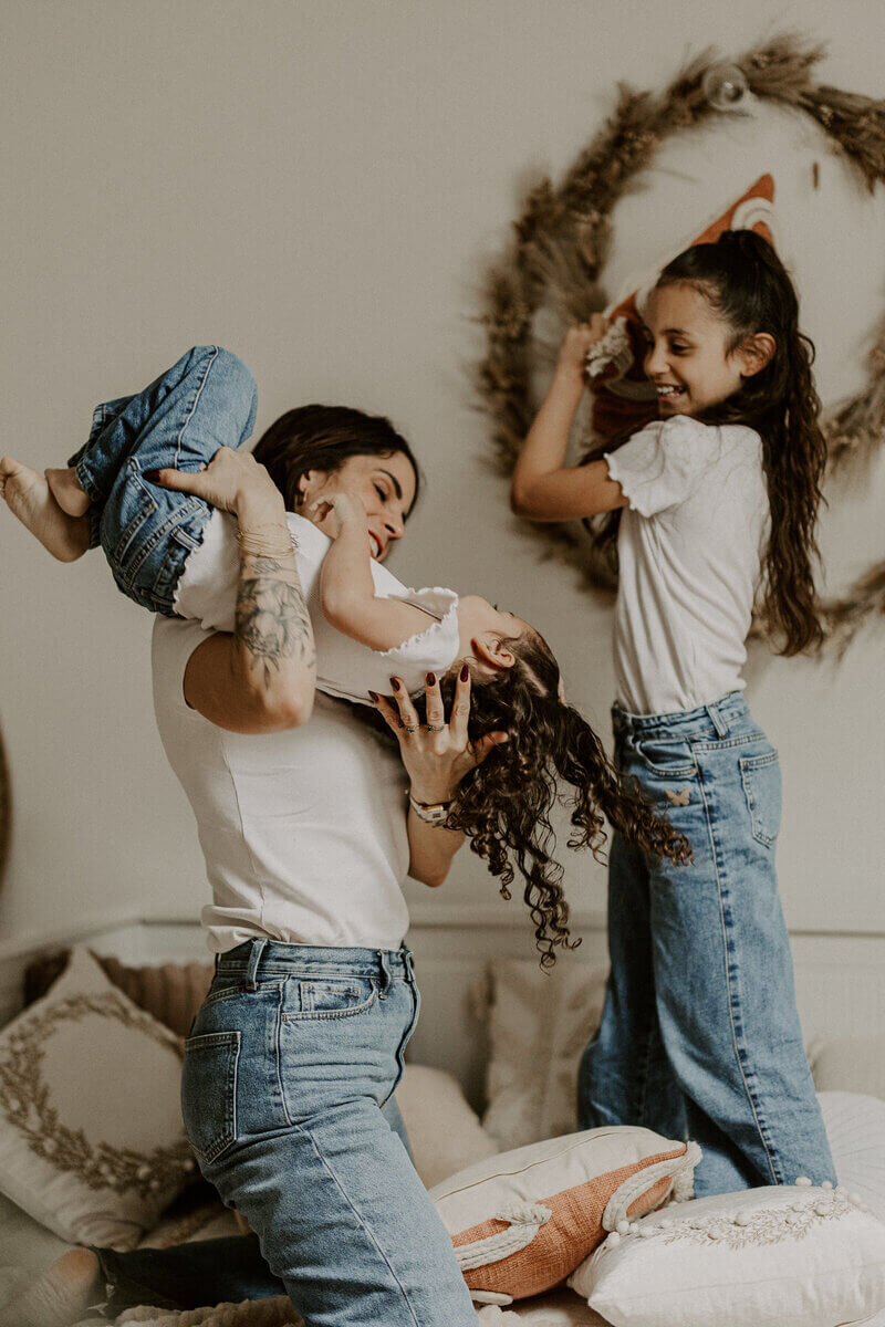 Maman jouant avec ses deux filles, habillées d'un jean et d'un haut blanc, dans un décor cosy au studio.