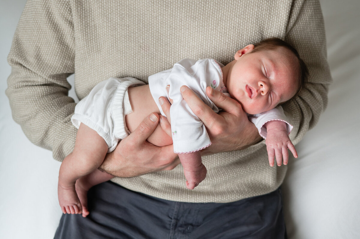 newborn baby with eyes closed, sleeping peacefully nestled on dad's arms