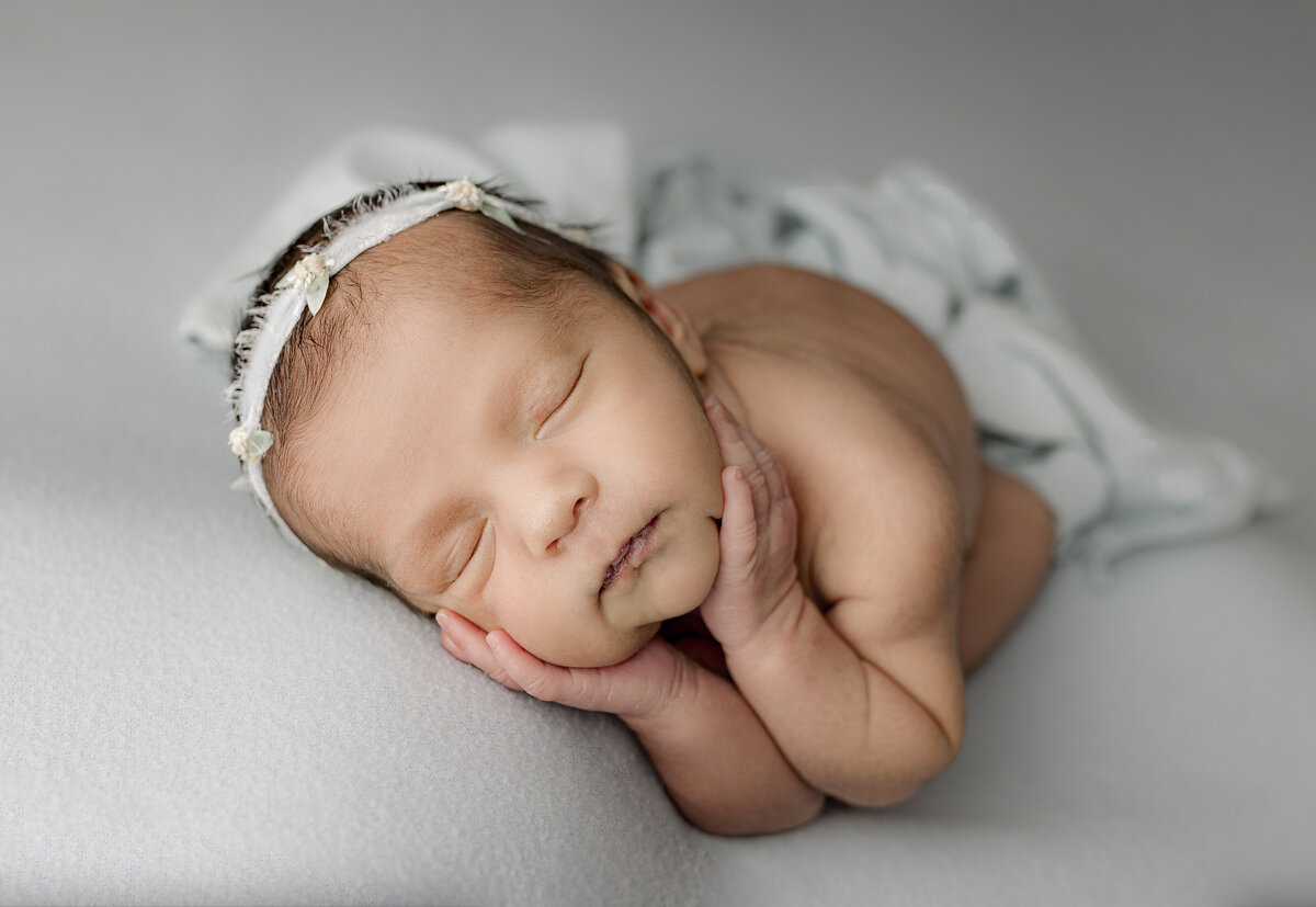 baby cupping cheeks on blue backdrop