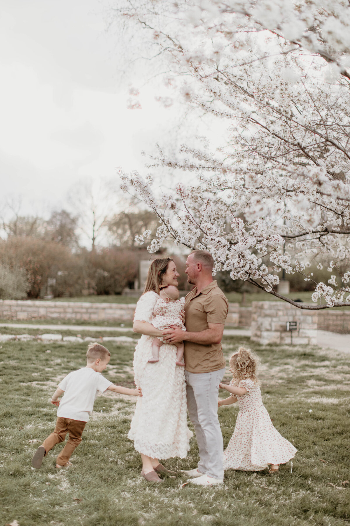 mom and dad in close embrace while two toddlers run around them. 