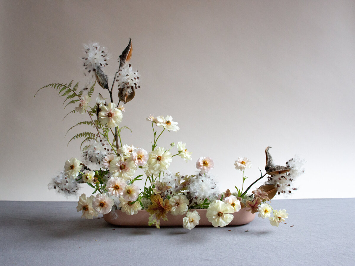 A modern floral arrangement of milkweed pods and organic flowers.