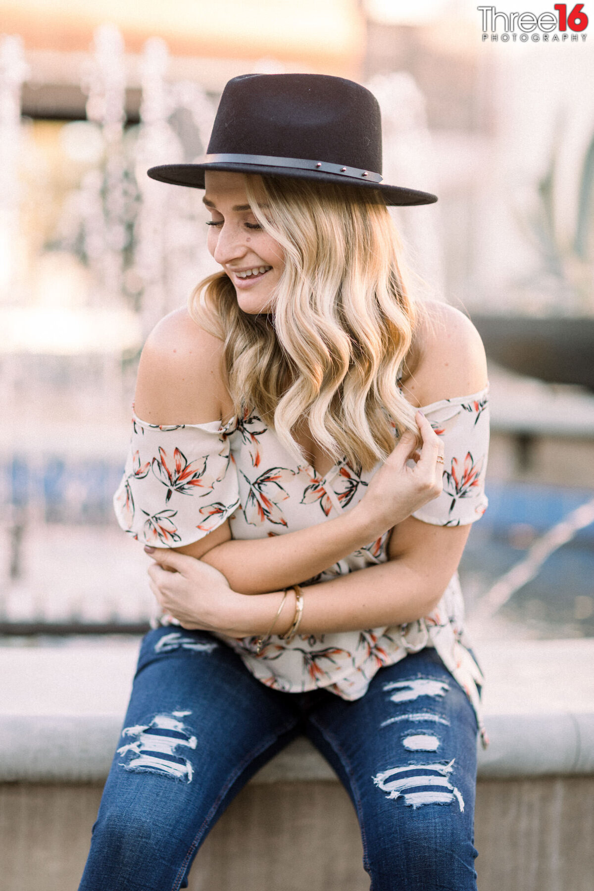 Woman in hat hugs herself and smiles during headshot photo session