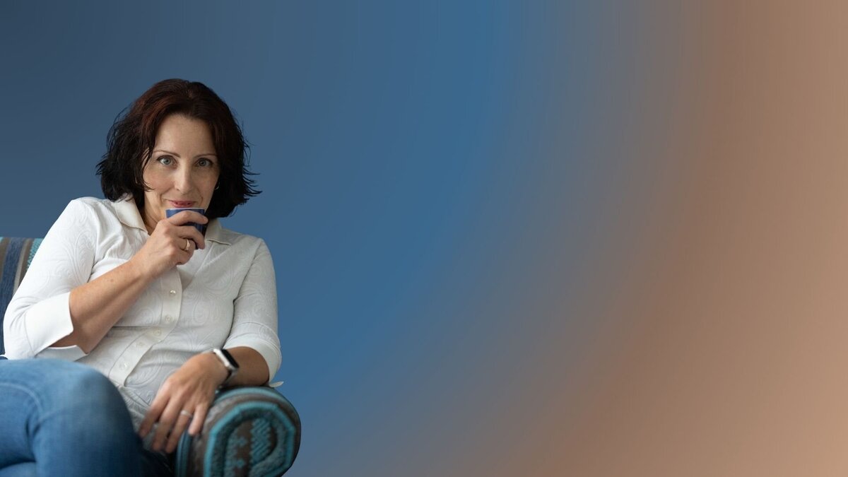 Csilla sitting in an armchair, looking at us over a cup of coffee. Relaxed and approachable.