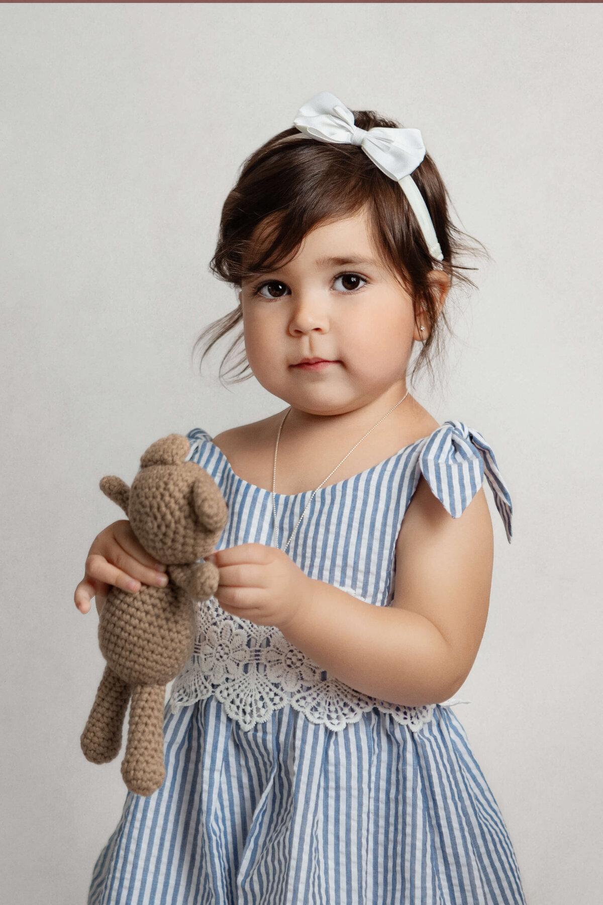 4 year old girl wearing a blue and white striped dress holding a brown bear