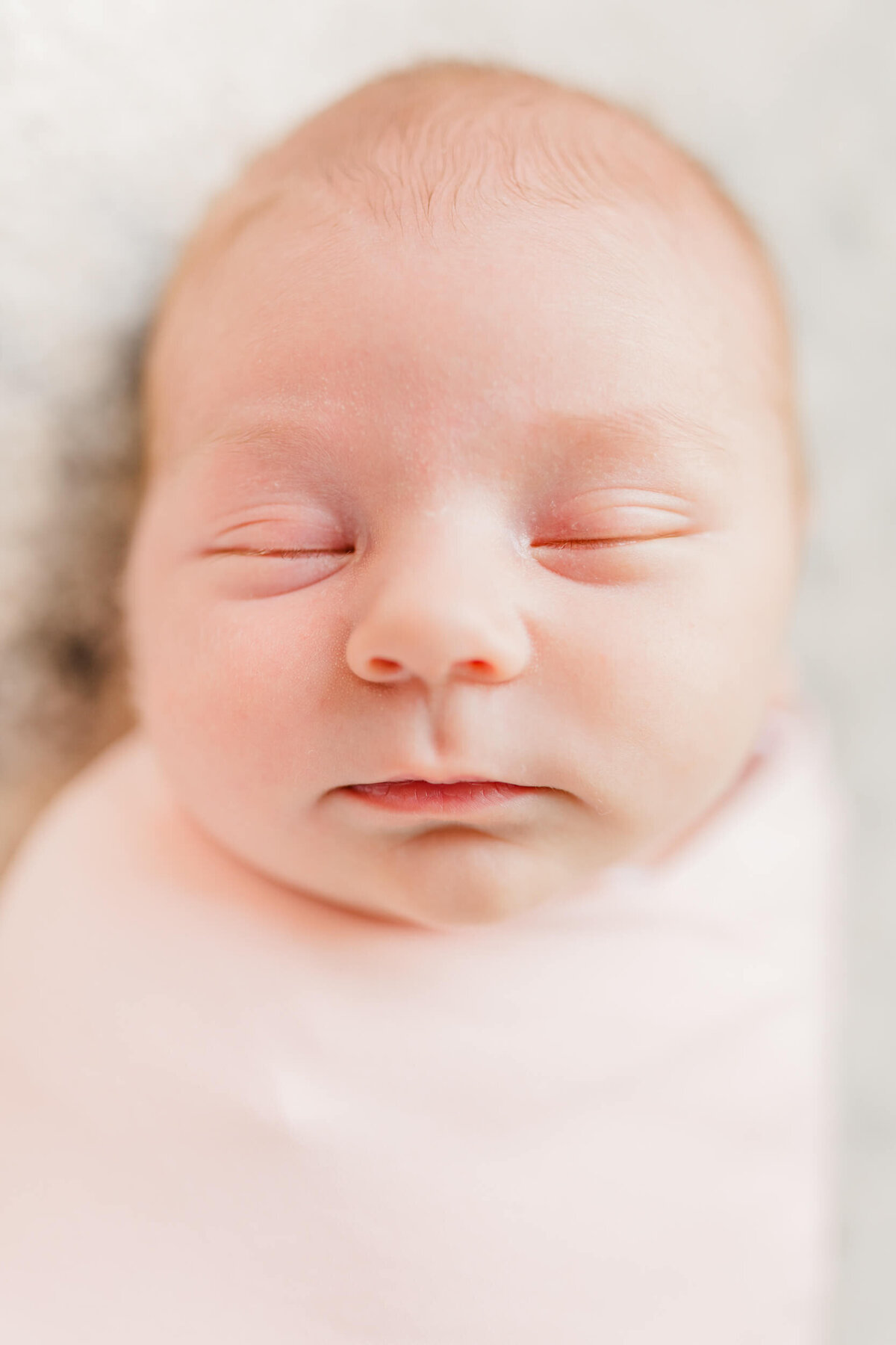 A sleeping newborn in a pink swaddle