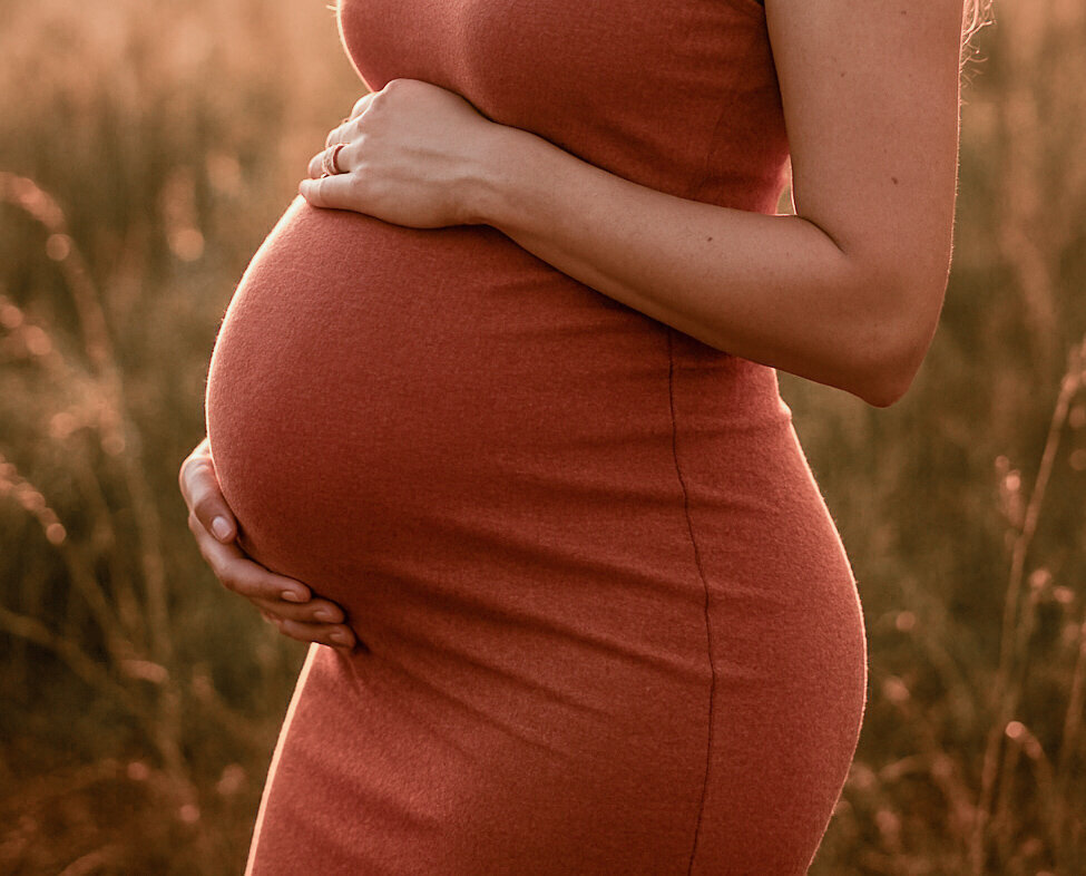 Mooie zwangere vrouw tijdens het gouden uur in het avondzonnetje die haar handen liefdevol op haar buik heeft.