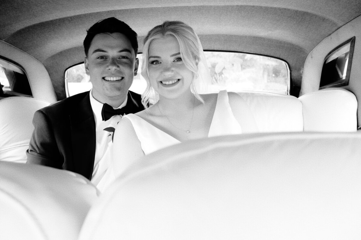 Bride and groom sitting in the back of their Rolls Royce wedding car looking at the camera and smiling