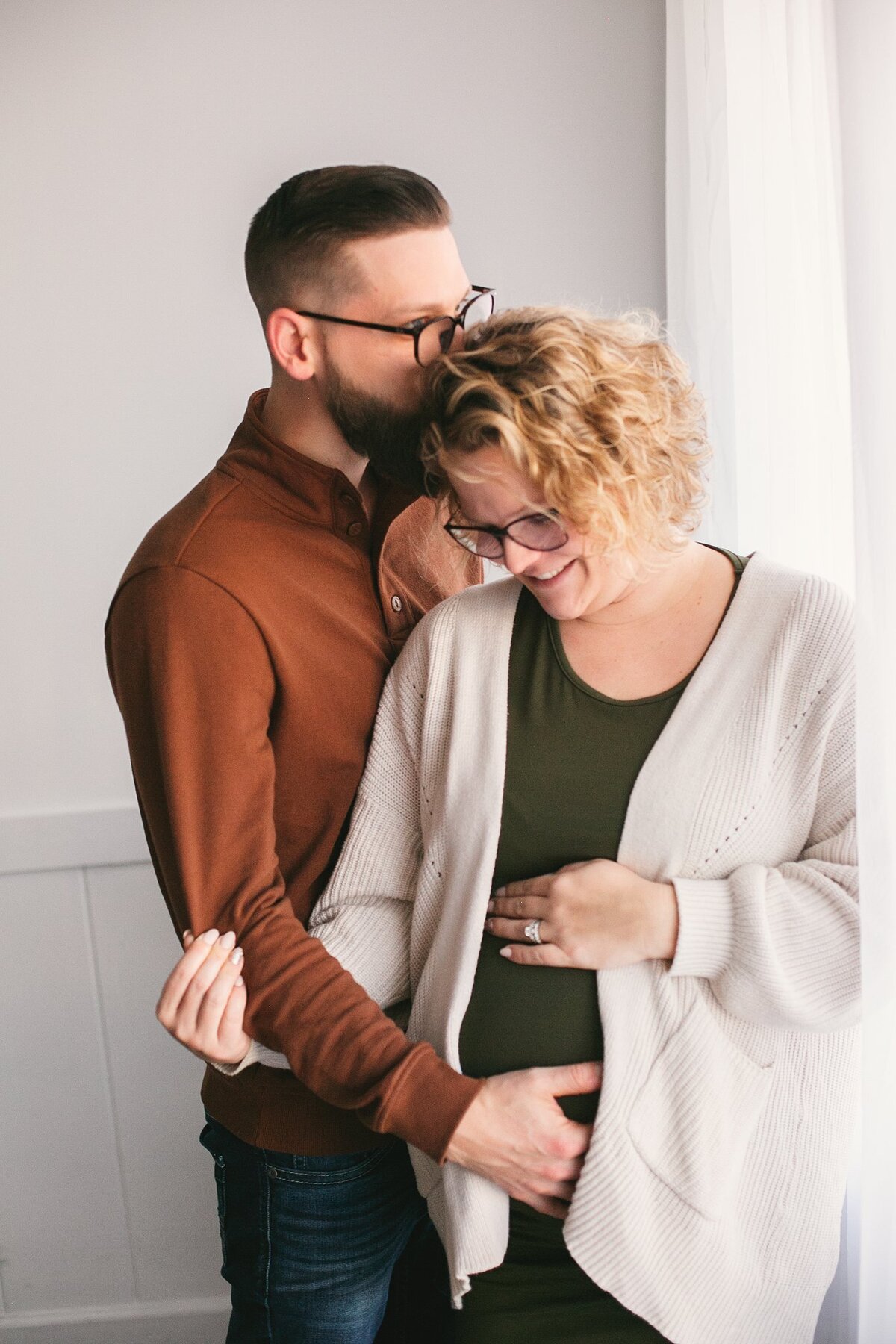 father-to-be-kissing-wife’s-forehead-as-they-hold-baby-bump-in-natural-light-maternity-session-in-indianapolis