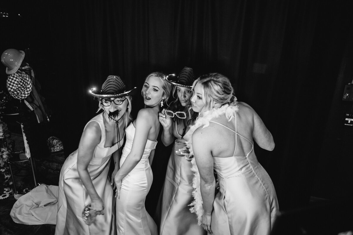 Black and white photo of the bride and bridesmaids in the photo booth wearing fun props and hats during the wedding reception at Old Edwards Inn in Highlands, North Carolina.