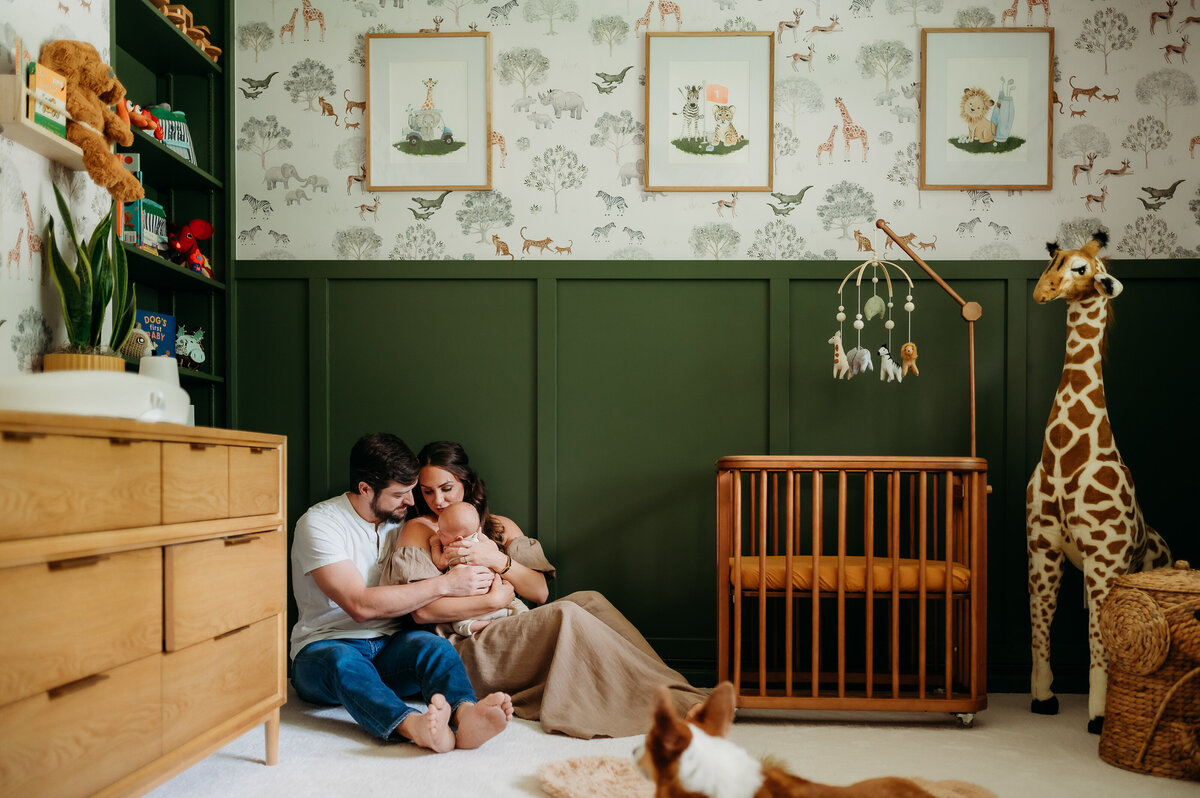 Artistic image of parents sitting on nursery floor with their baby next to the crib, sitting in beautiful light while holding their sleeping baby in Timonium Maryland