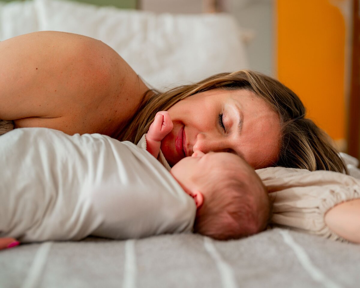 woman lying on bed next to baby