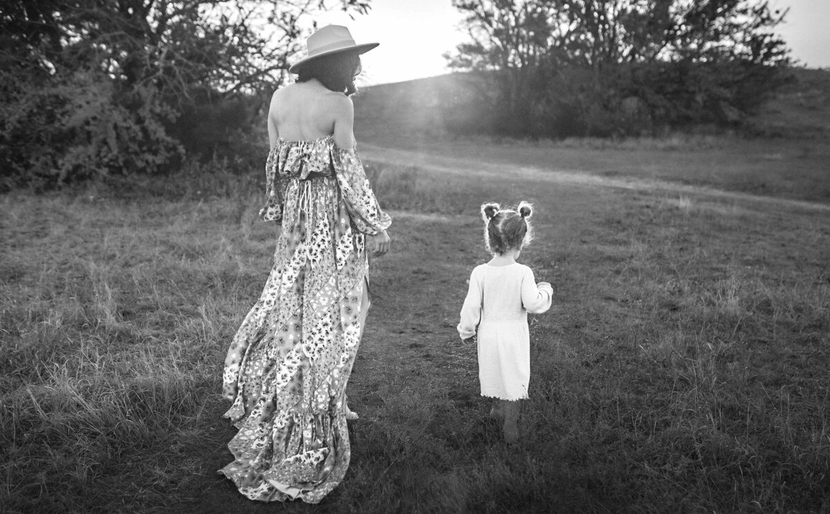 A woman is walking with her young daughter. You cna only see their backs and the sunset