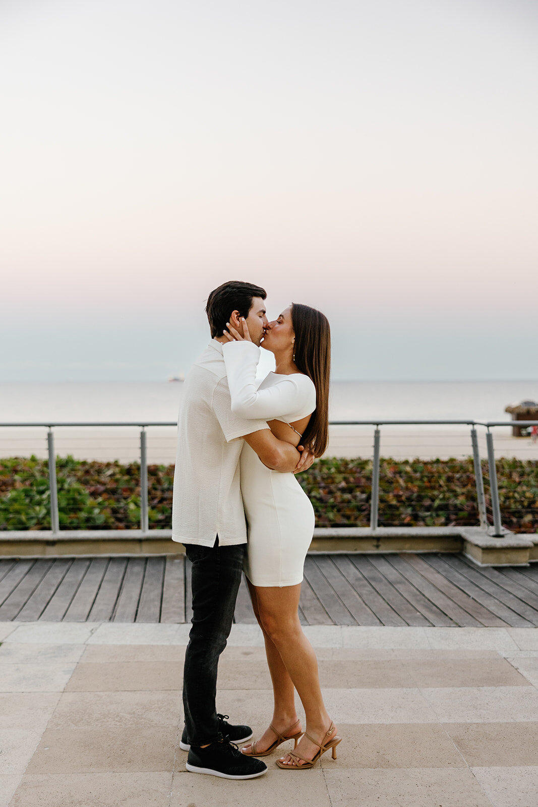 The engaged couple stands near the ocean, embracing each other as the soft pastel hues of the sky paint a romantic backdrop for their Marriott Hotel Fort Lauderdale engagement session.