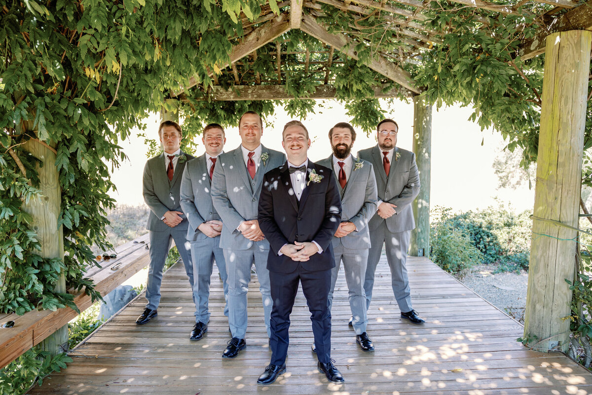 groom and his groomsmen standing in an outdoor pergola with lush vine overhead at Rosewood Events photographed by wedding photographer bay area