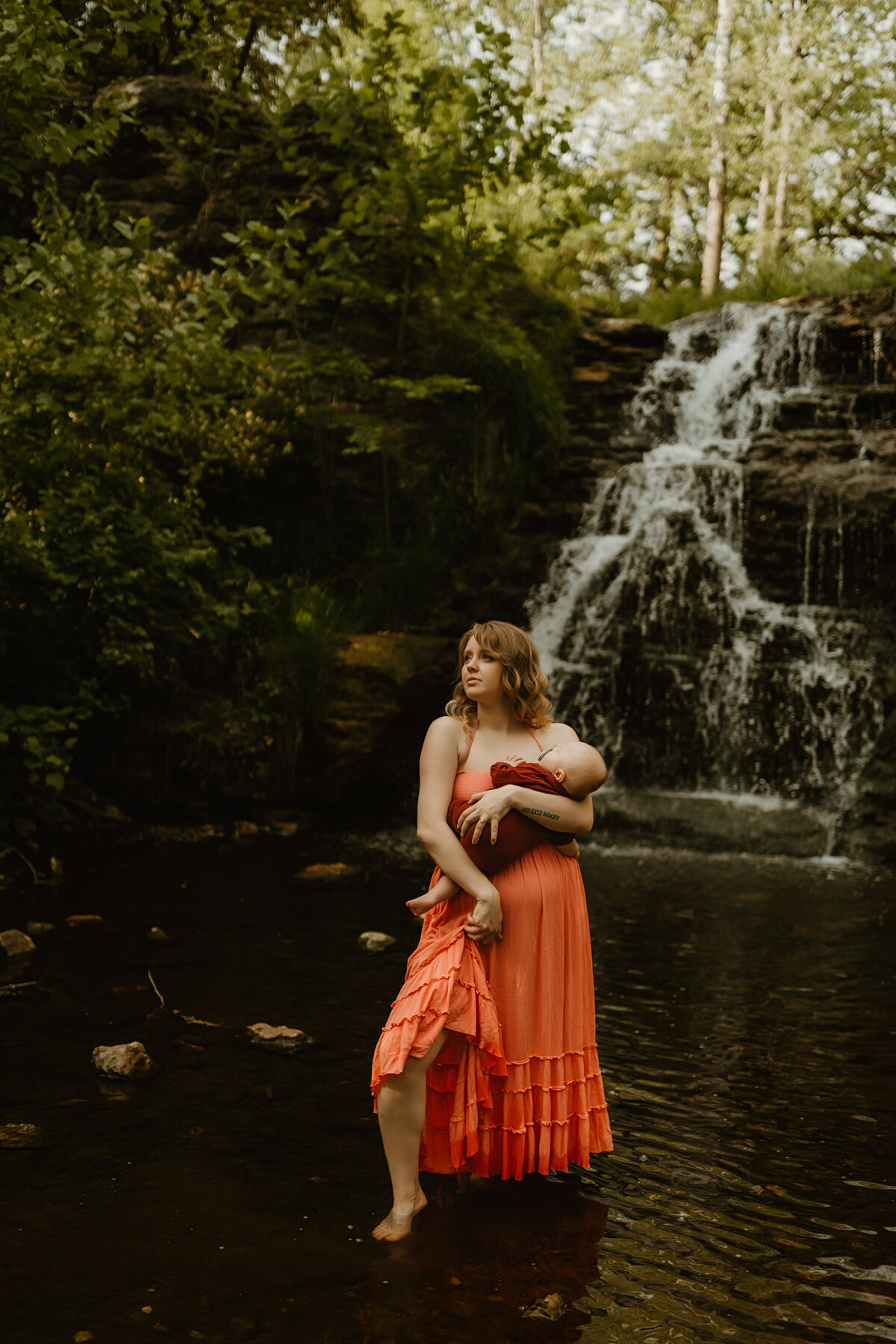 mom and baby pose in creek near waterfall at photoshoot in indiana