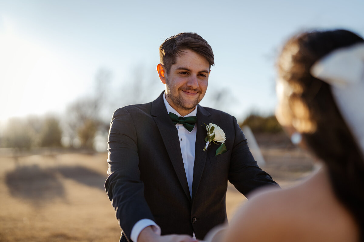 Groom smiling tenderly as he holds his bride's hands during a winter wedding at D'Vine Grace Vineyard. The soft sunset in the background adds warmth and romance to this intimate moment.