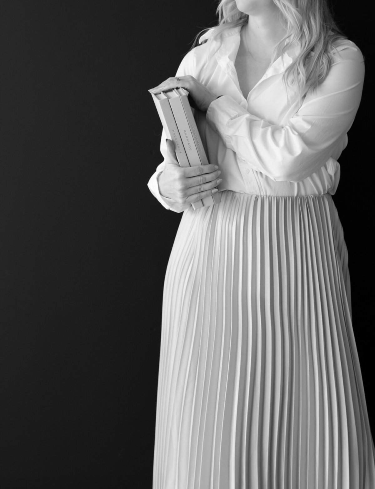 woman in light pleated skirt holds journals, black studio backdrop