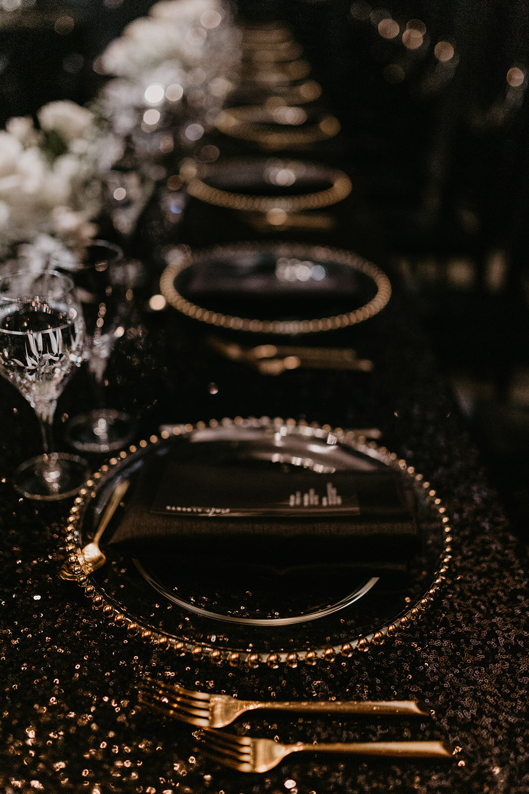 Black and gold dressed table with white floral centerpieces at wedding reception.