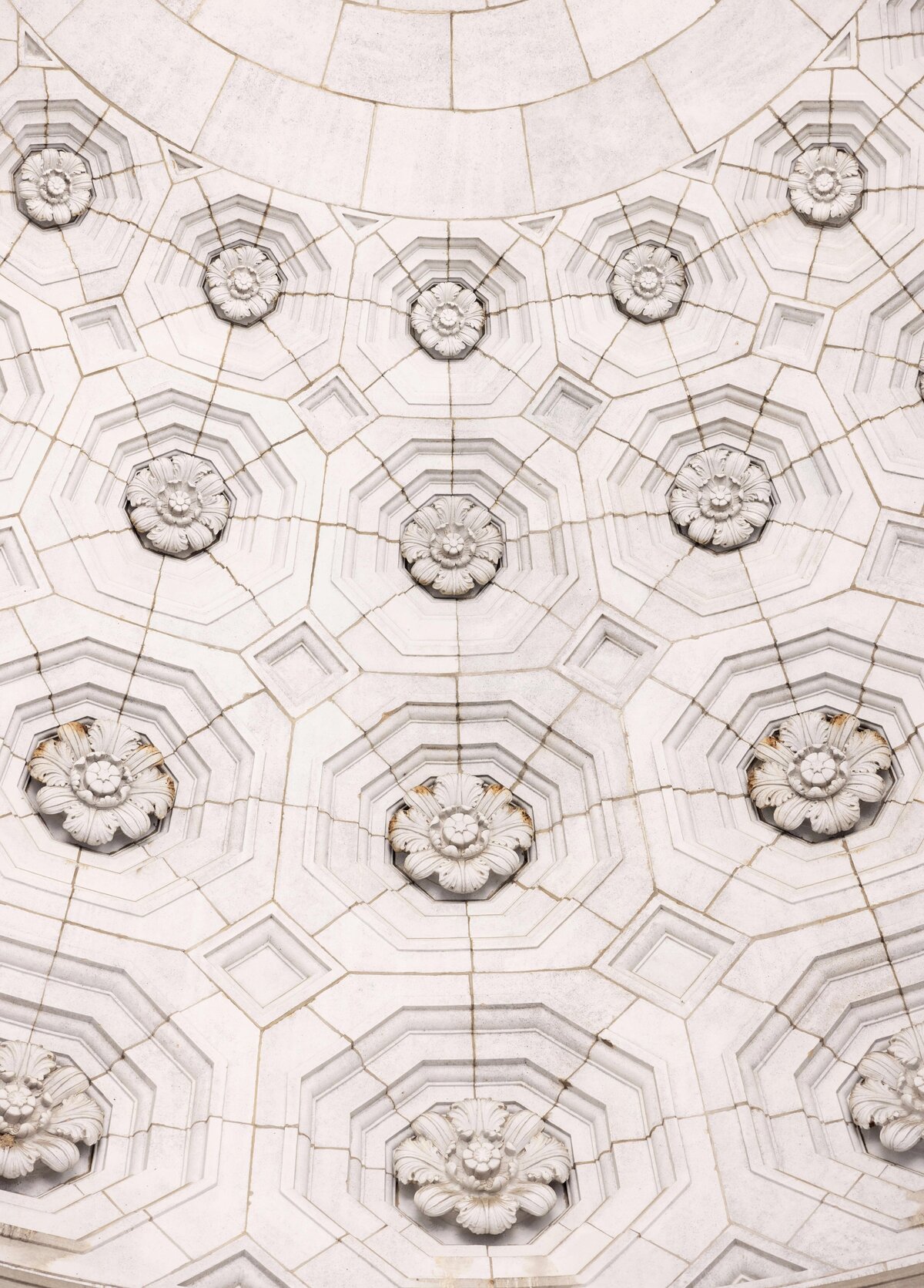 Close-up of an ornate, geometric architectural ceiling featuring rows of hexagonal and octagonal tiles with floral motifs in the center. The design is symmetrically arranged, showcasing intricate stone carvings and a light color palette.