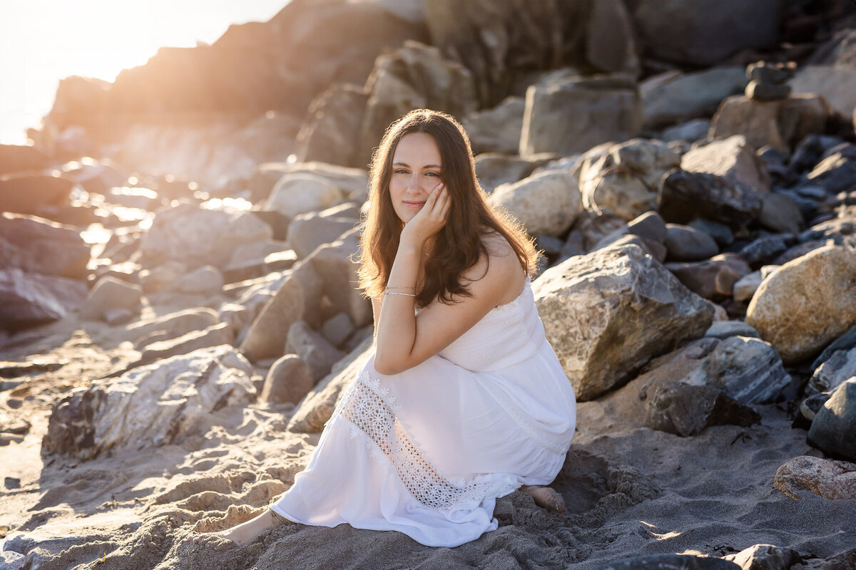 high school senior sitting on rocks at beach in a white dress by nh senior photographer lisa smith photography