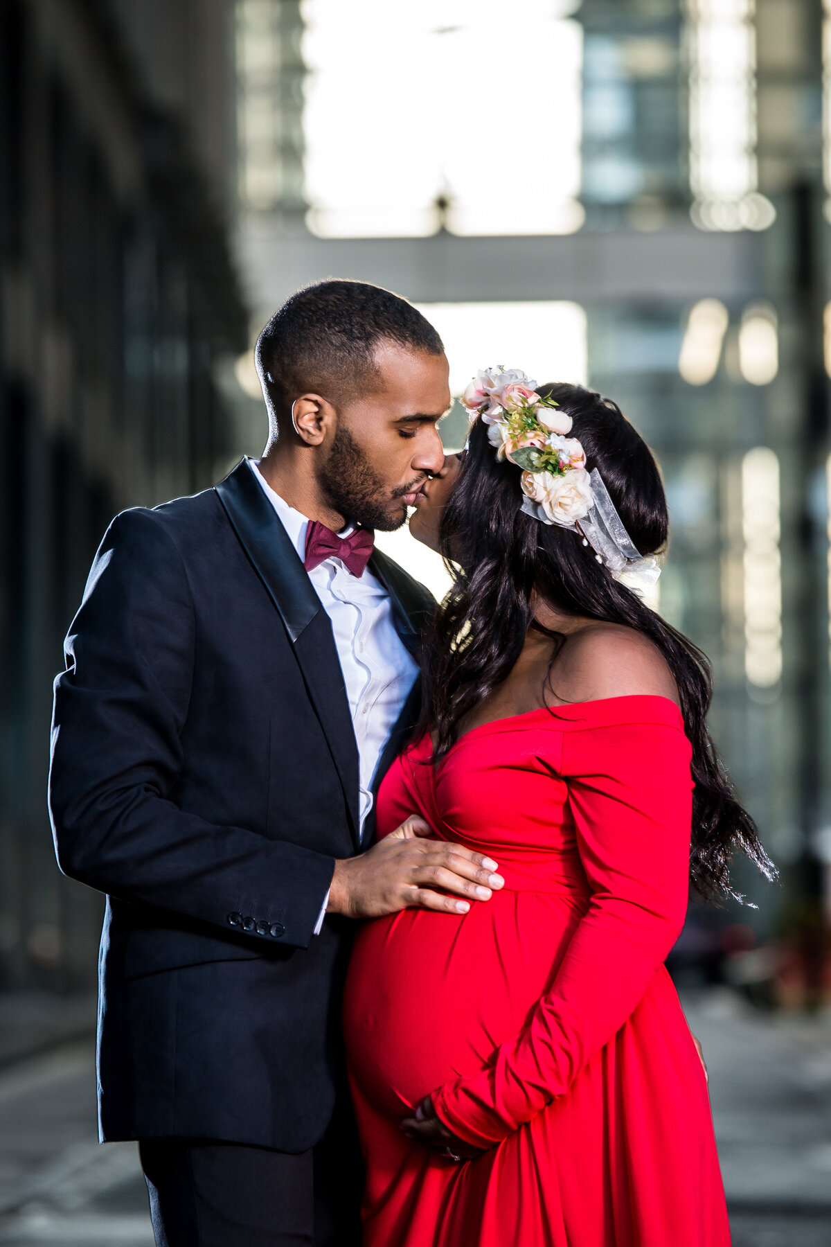 a Black couple pose together, wearing red and blue. She wears a flower crown made of white rose  buds