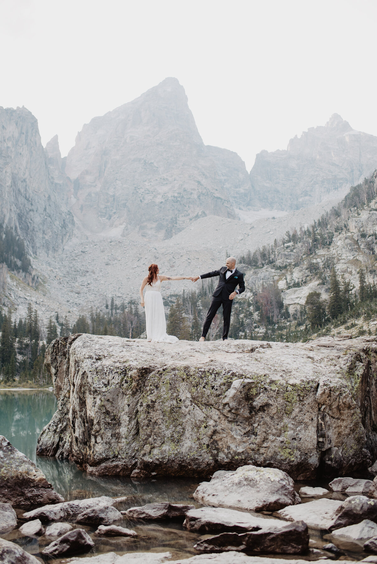 Jackson Hole photographers capture bride and groom pulling one another on boulder