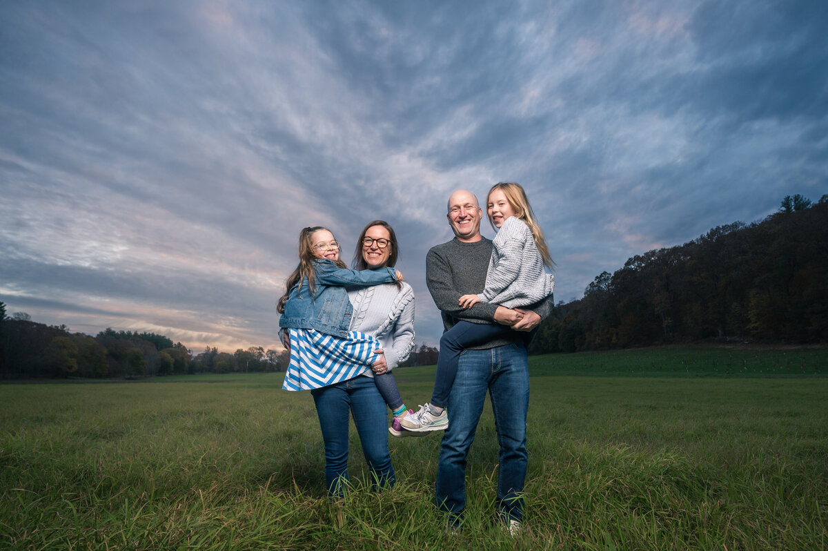 Family of 4 holding girls at dusk with dramatic clouds