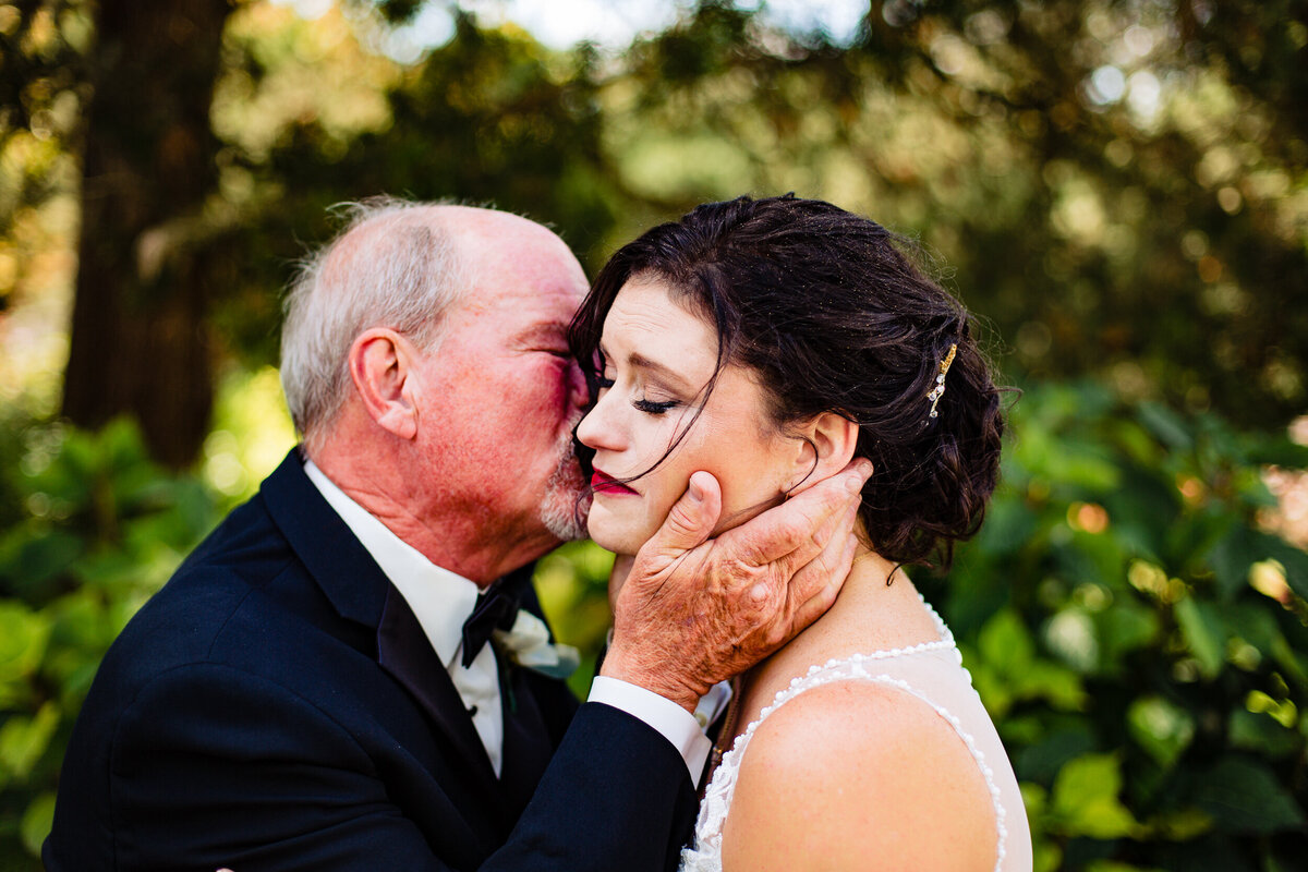One of the top wedding photos of 2020. Taken by Adore Wedding Photography- Toledo, Ohio Wedding Photographers. This photo is of a bride and her father as he kisses her on the cheek as the two cry together during a first look in the garden of the Toledo Zoo