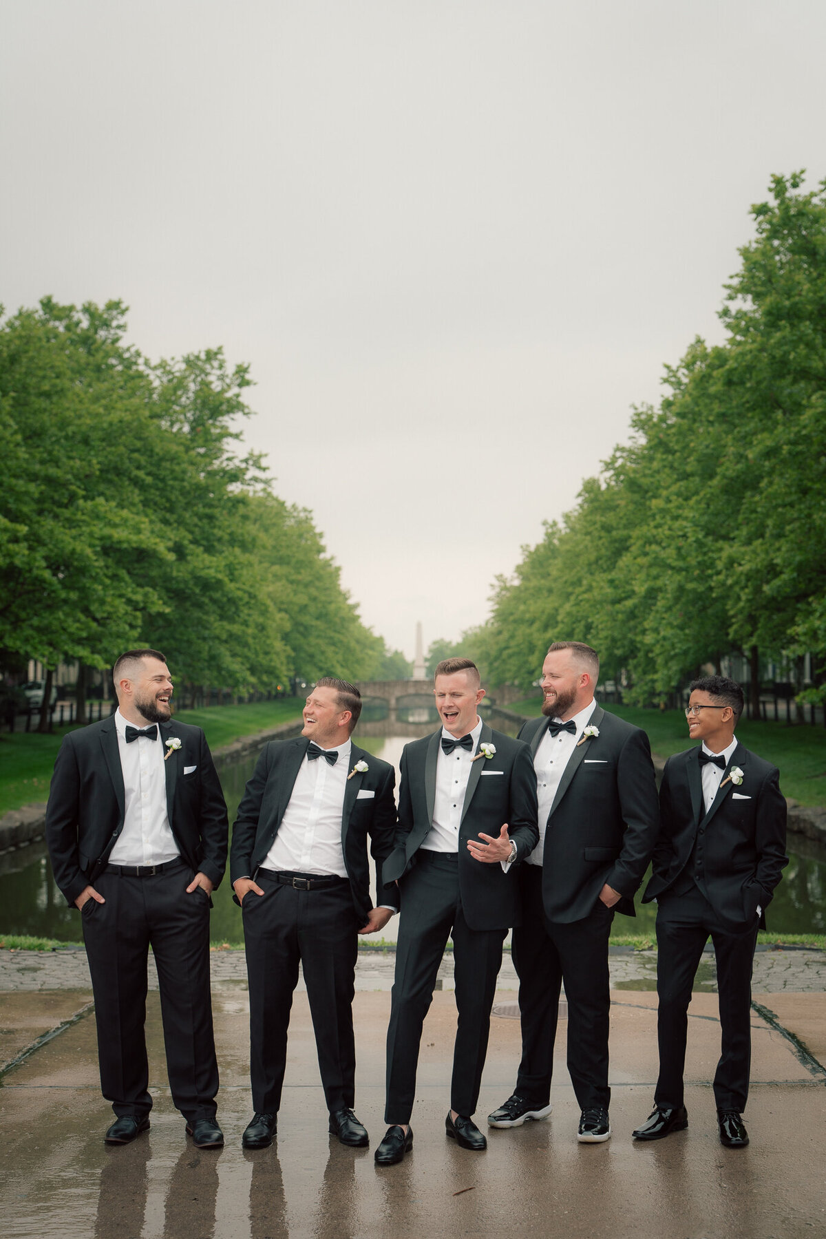Groom with groomsmen laughing outdoors by canal