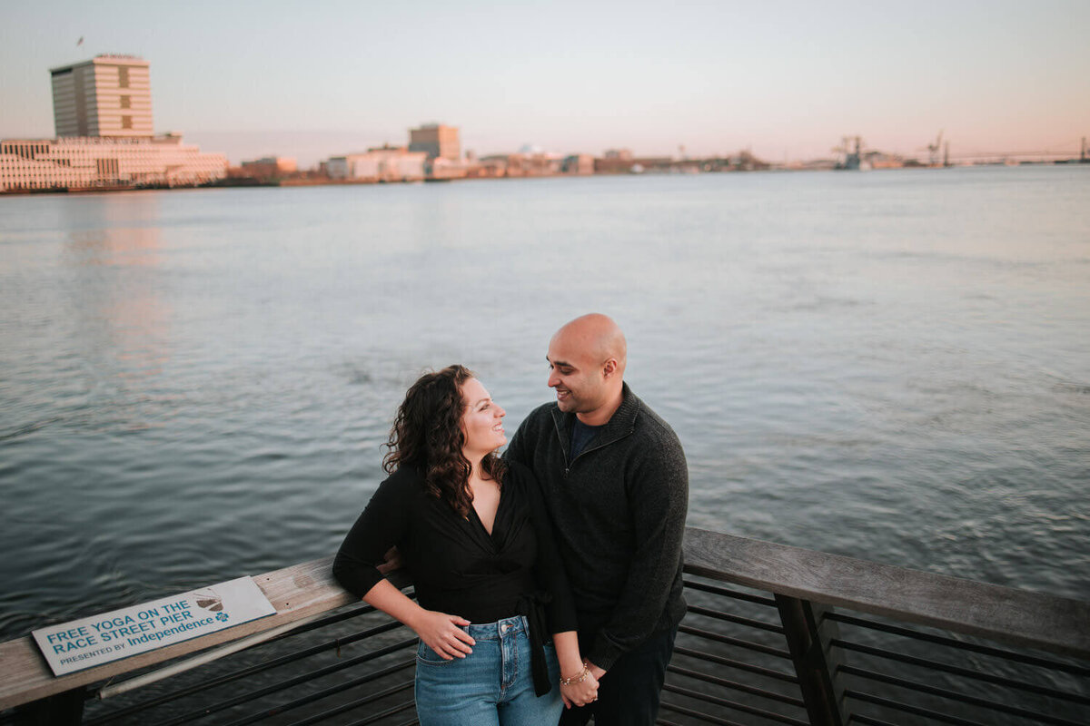 A couple shares a joyful moment at Race Street Pier in Philadelphia, with the waterfront skyline in the background