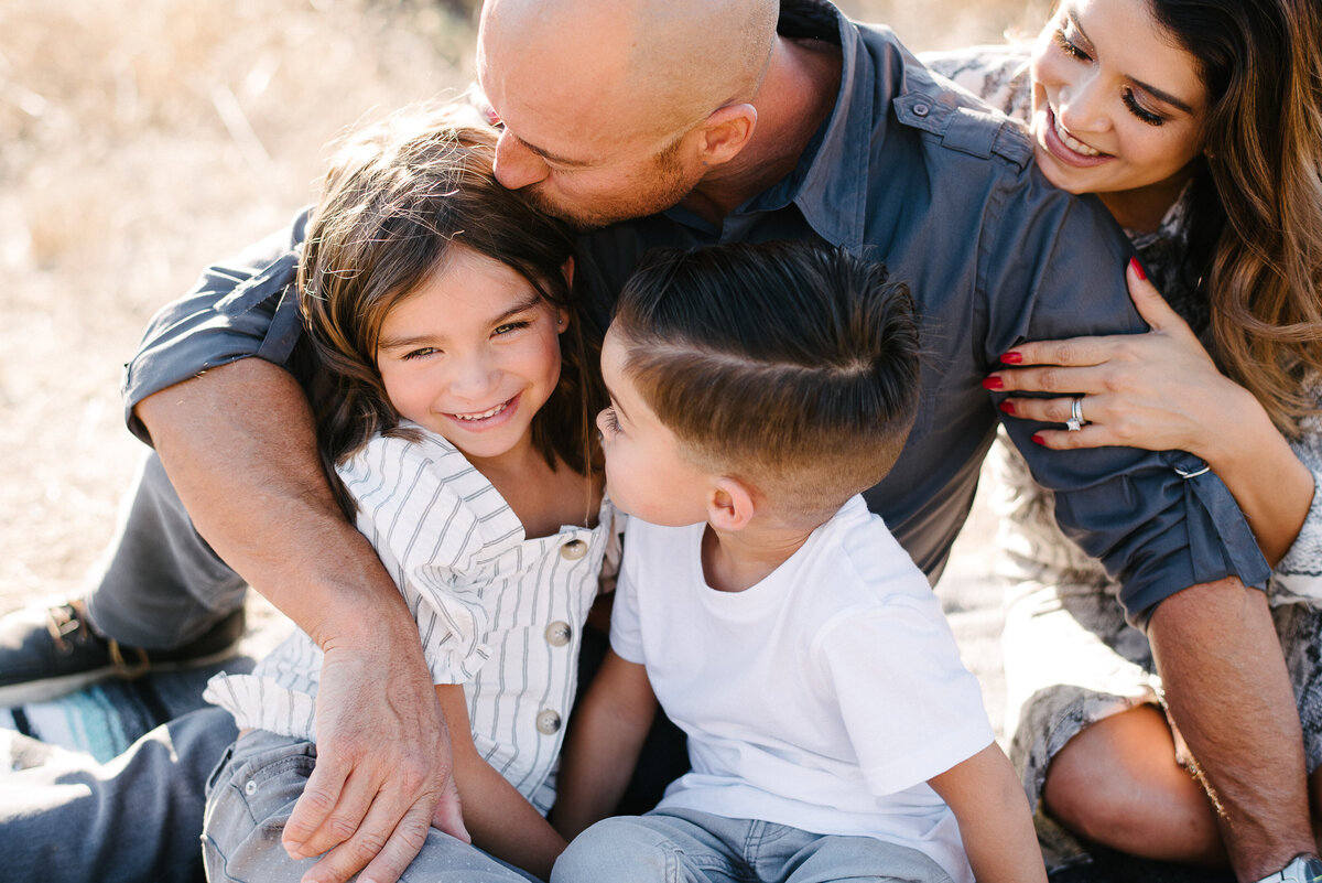 San Diego Family snuggles while Dad gives his daughter a kiss on her head