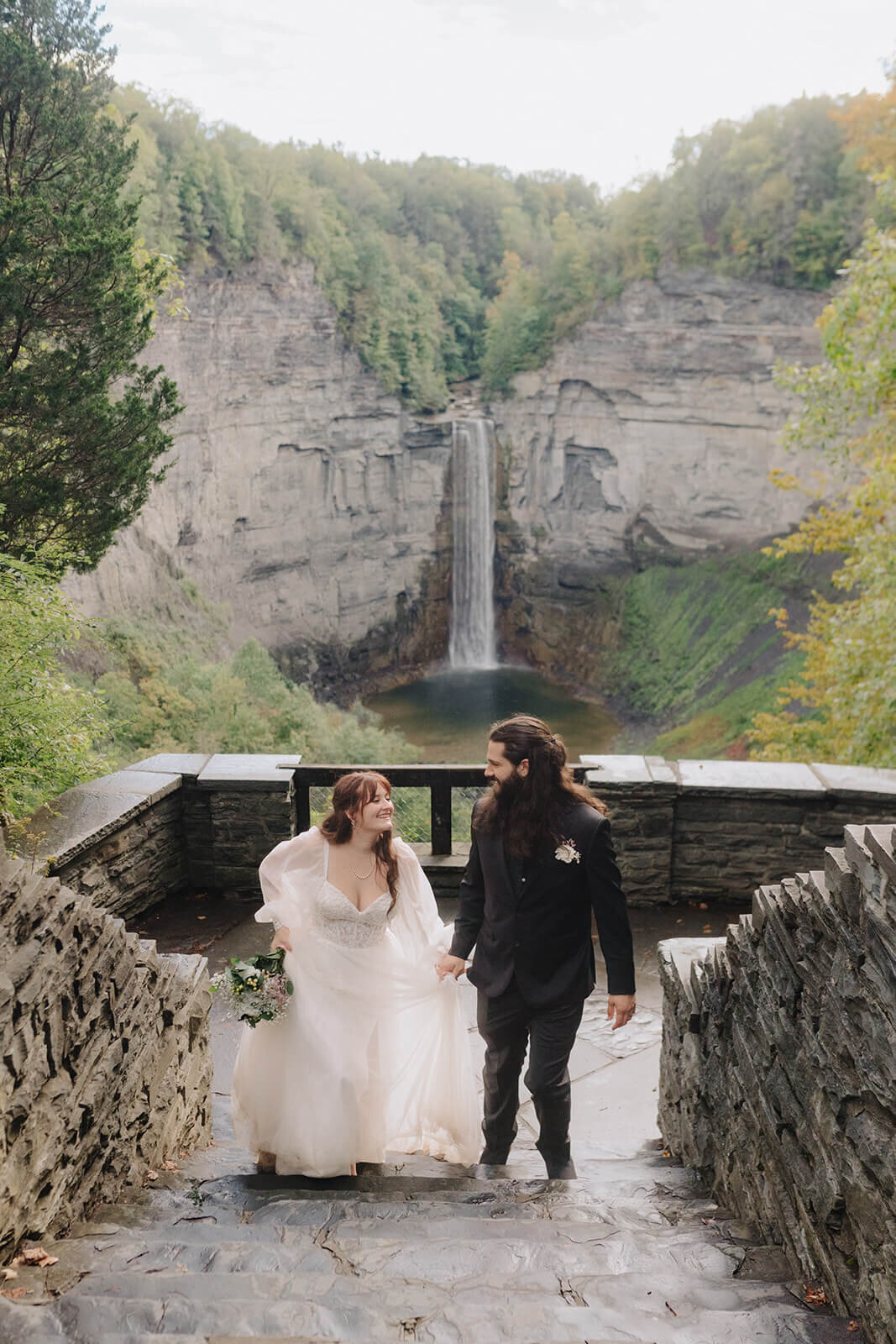 bride and groom walking up steps with waterfall in the background